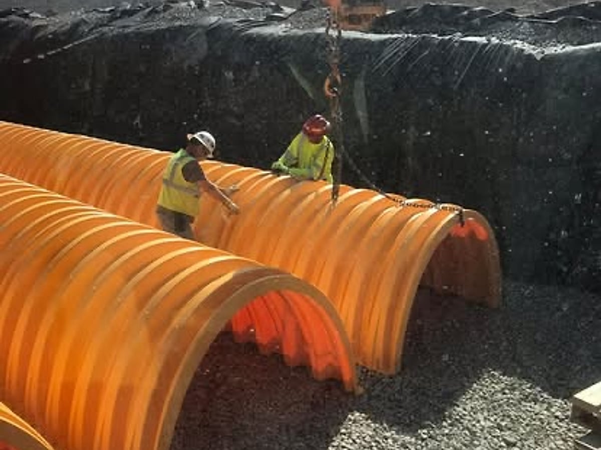Crew placing large arch culvert pipe into a lined basin