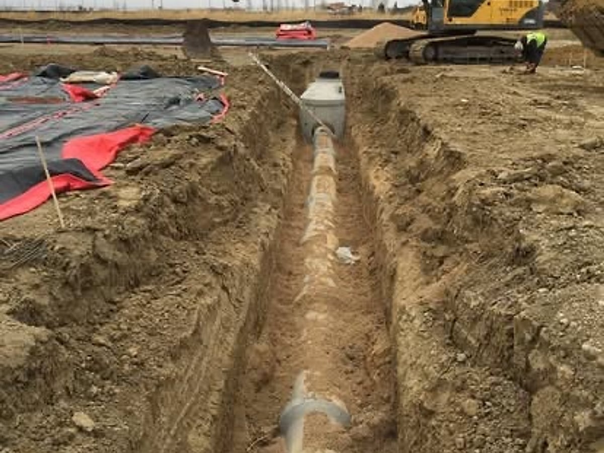 Excavator digging an open utility trench with pipe laid in on an Arizona commercial site