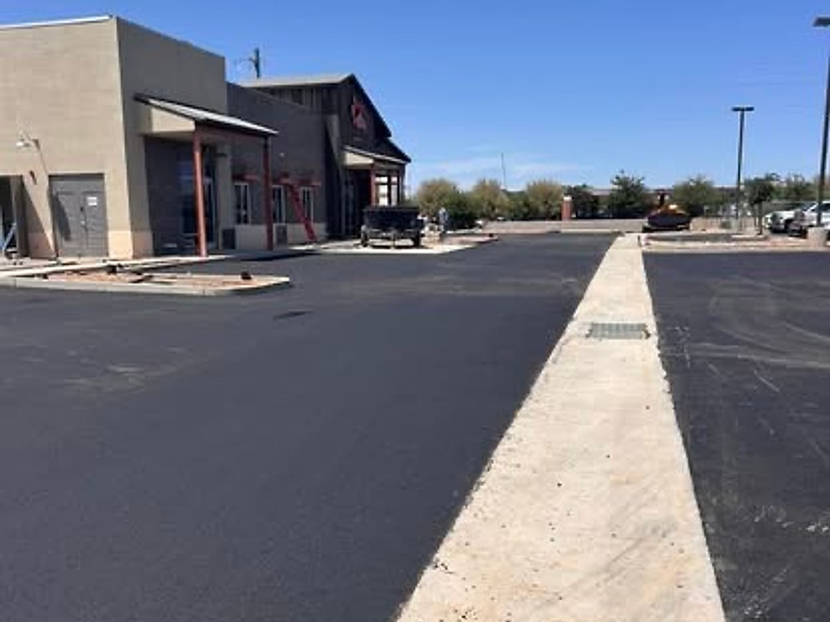 Freshly paved asphalt drive lane with a new concrete curb at a commercial site